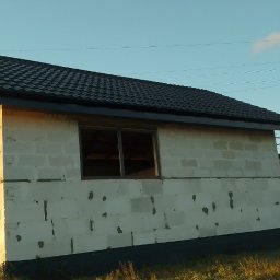 SIM DIM House - Niedokończony budynek w trakcie budowy, z czarnym dachem z blachodachówki, oknami bez szyb, oraz rusztowaniem z boku, na tle błękitnego nieba i zielonego krajobrazu.
