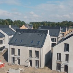 SIM DIM House - Nowe domy szeregowe z ciemnymi dachami i oknami dachowymi, widoczne prace wykończeniowe na zewnątrz, gruz w czerwonym kontenerze.