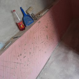 Raf bud - Ściana przygotowana do dalszych prac wykończeniowych, z widocznymi śladami po szpachlowaniu i rysami, obok leżą narzędzia: szpachelka, pędzel, nożyki oraz butelka z napojem.