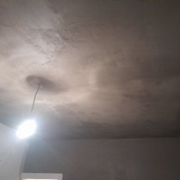 Raf bud - Niedokończony sufit po nałożeniu warstwy szpachli, widoczna wisząca żarówka i fragment ściany w szarym odcieniu.