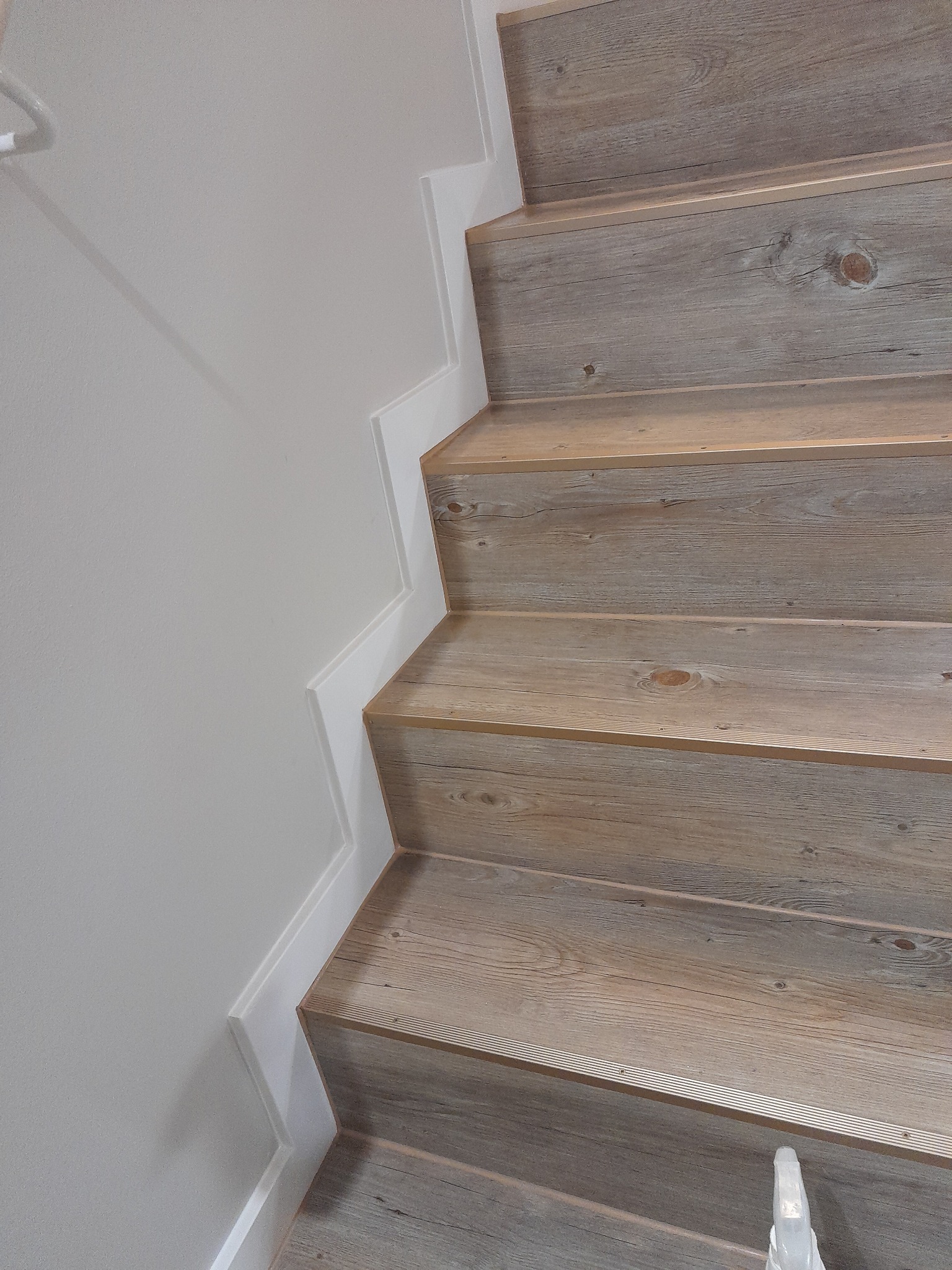 Schody wykończone panelami imitującymi drewno, z białymi listwami przypodłogowymi, widoczne z góry pod kątem.