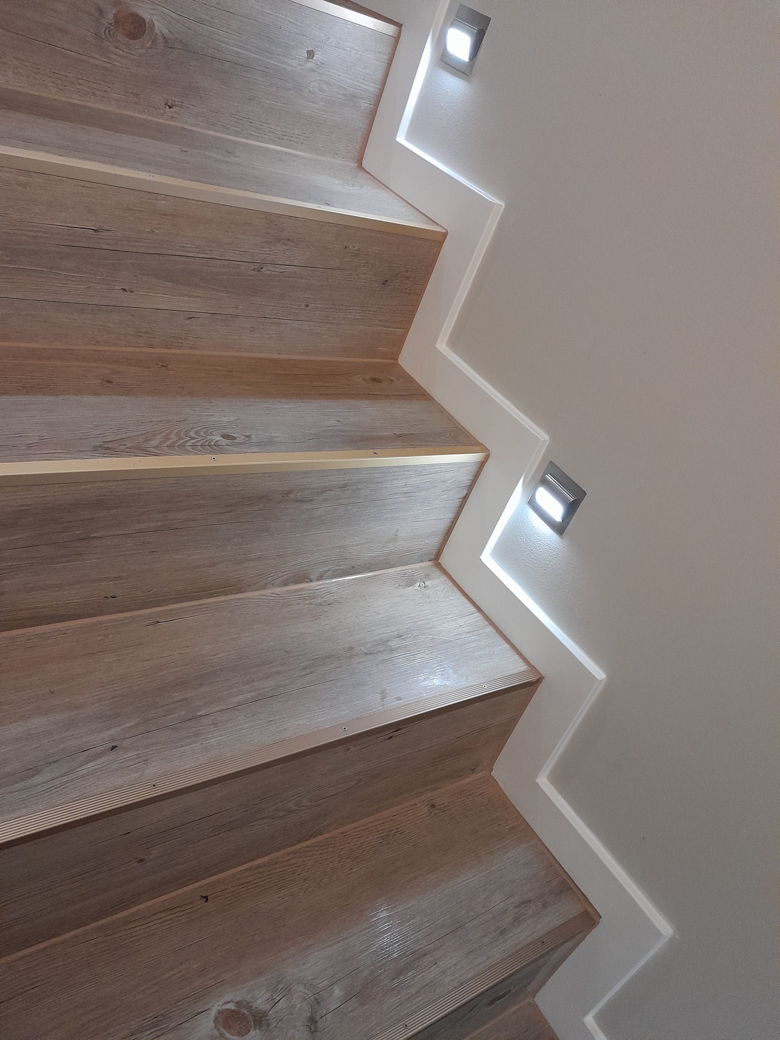 Schody wyłożone panelami drewnopodobnymi z oświetleniem punktowym przy ścianie.