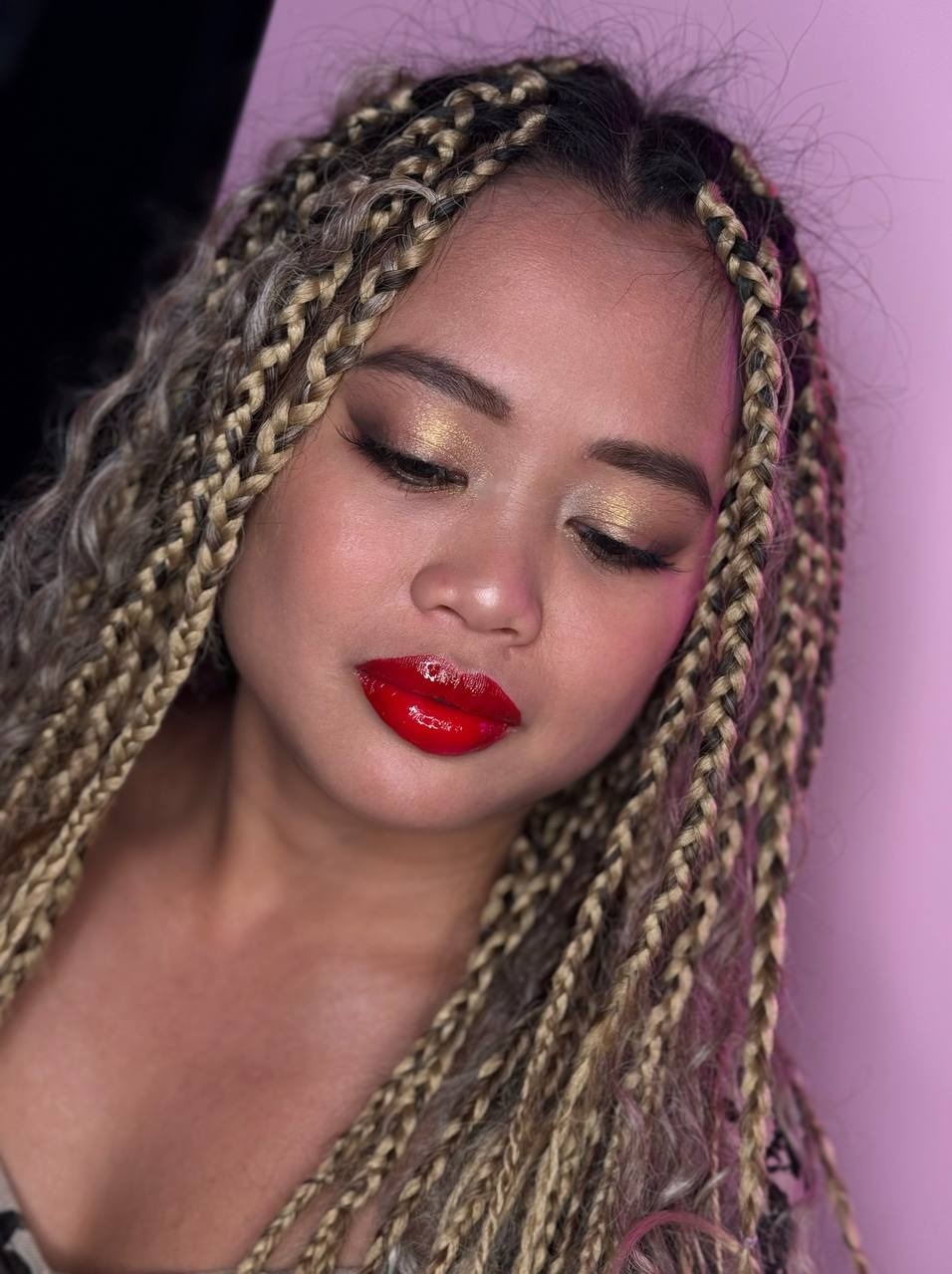 Portret kobiety z błyszczącym, czerwonym makijażem ust i złotym cieniem na powiekach, z warkoczami blond i brąz.