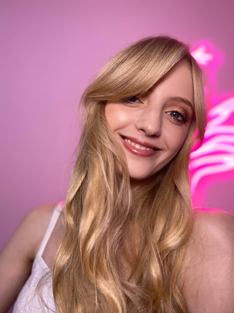 Portret uśmiechniętej blondynki z delikatnym, błyszczącym make-upem oczu i ust na tle neonowego różu.