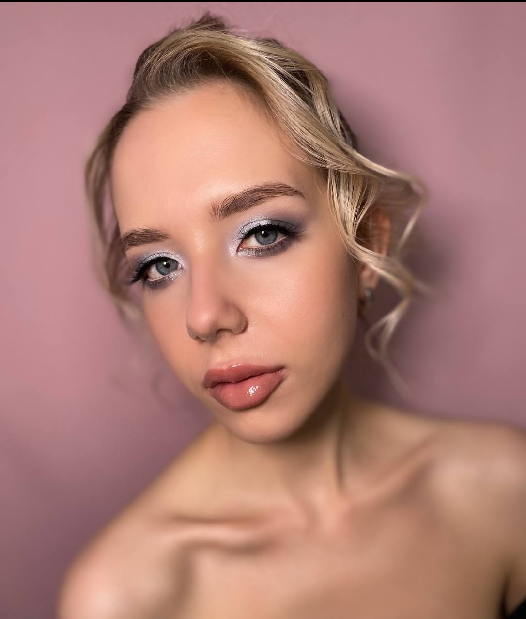 Portret kobiety z delikatnym, srebrzysto-szarym cieniowaniem powiek i błyszczącymi ustami, wykonanym we Wrocławiu, na tle pudrowego różu.