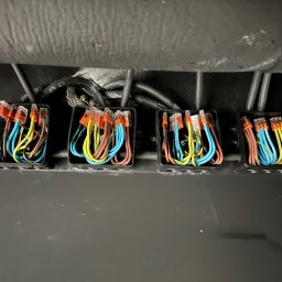 Damian Rojek - Cztery czarne puszki z kolorowymi przewodami (żółty, niebieski, brązowy) połączonymi złączkami Wago, zamontowane na szarej powierzchni. Widoczne kable w górnej części.