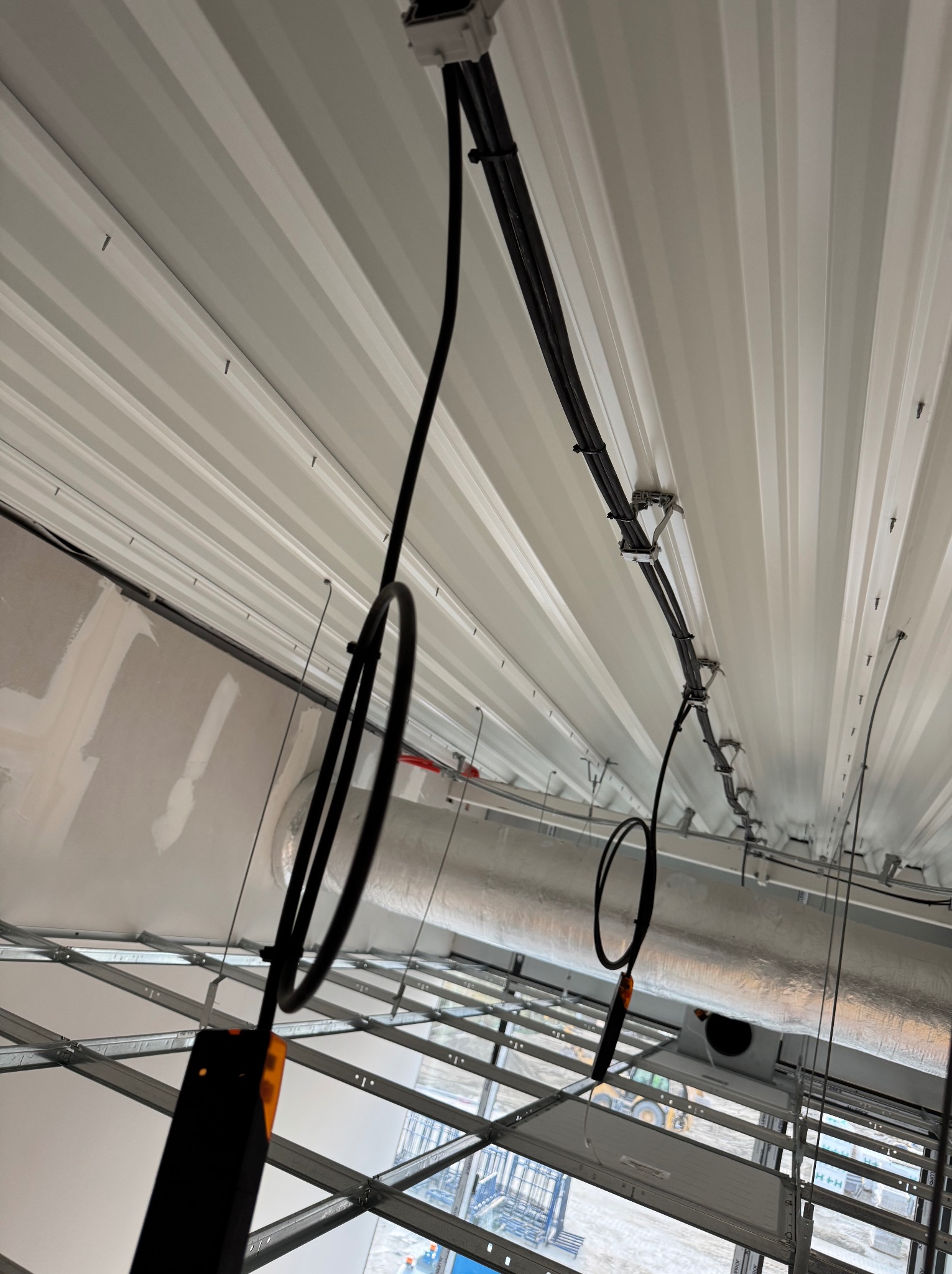 Biały sufit z widocznymi kablami i elementami instalacji. Kable przymocowane do sufitu za pomocą uchwytów. Widok z dołu, perspektywa zniekształcona.