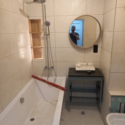 Łazienkowe Love - Przystępne cenowo i stylowo - Biała łazienka w trakcie prac wykończeniowych, poziomica oparta o wannę, w lustrze odbicie osoby robiącej zdjęcie.