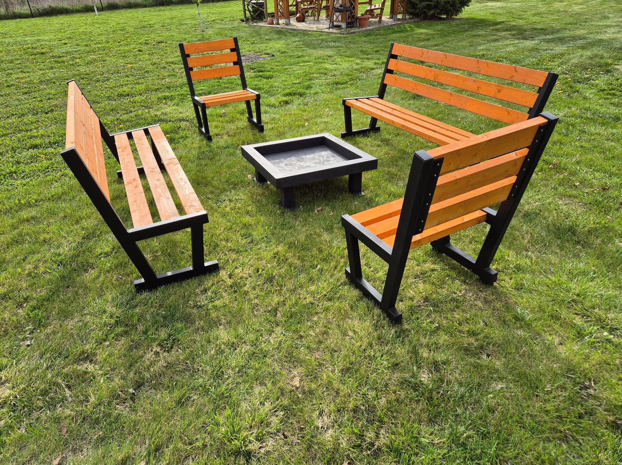 Komplet mebli ogrodowych: dwie ławki i dwa krzesła z drewna i metalu, ustawione wokół paleniska na trawniku. Nowoczesny design, czarne ramy, pomarańczowe deski.