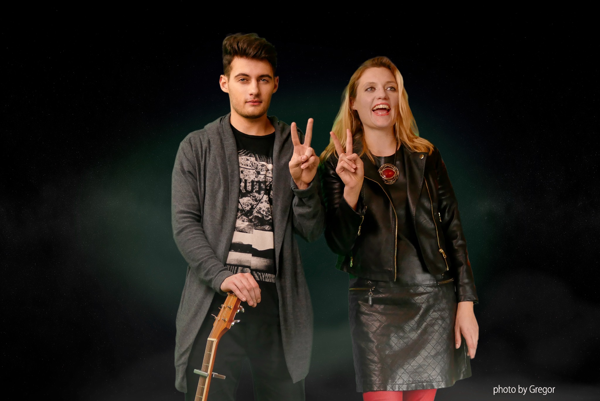 Młody mężczyzna trzyma gitarę, obok stoi uśmiechnięta kobieta w skórzanej kurtce, oboje pokazują znak zwycięstwa na tle ciemnego, gwieździstego tła.