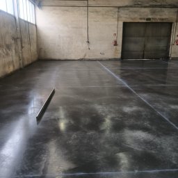 ROB-BET Grzegorz Słupiński - Świeżo wylana, ciemnoszara posadzka w hali przemysłowej, widoczne linie podziału i poziomica leżąca na powierzchni.