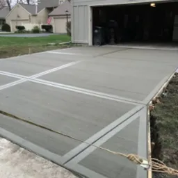 Nowy betonowy podjazd do garażu z widocznymi dylatacjami i świeżo usuniętymi elementami szalunku, teren wokół jeszcze niezagospodarowany.