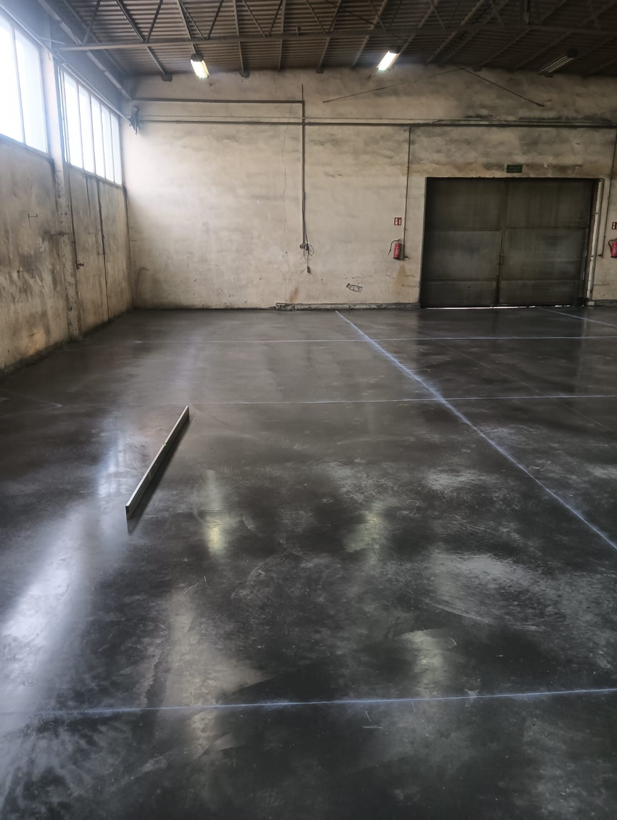 Świeżo wylana, ciemnoszara posadzka w hali przemysłowej, widoczne linie podziału i poziomica leżąca na powierzchni.