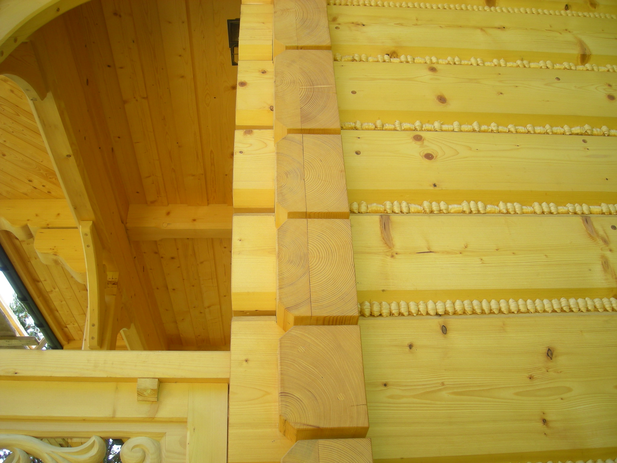 Fragment drewnianej konstrukcji domu z bali, widoczne połączenia bali z użyciem drewnianych kołków, detale ciesielskie i wykończenie elewacji z dekoracyjnymi elementami.