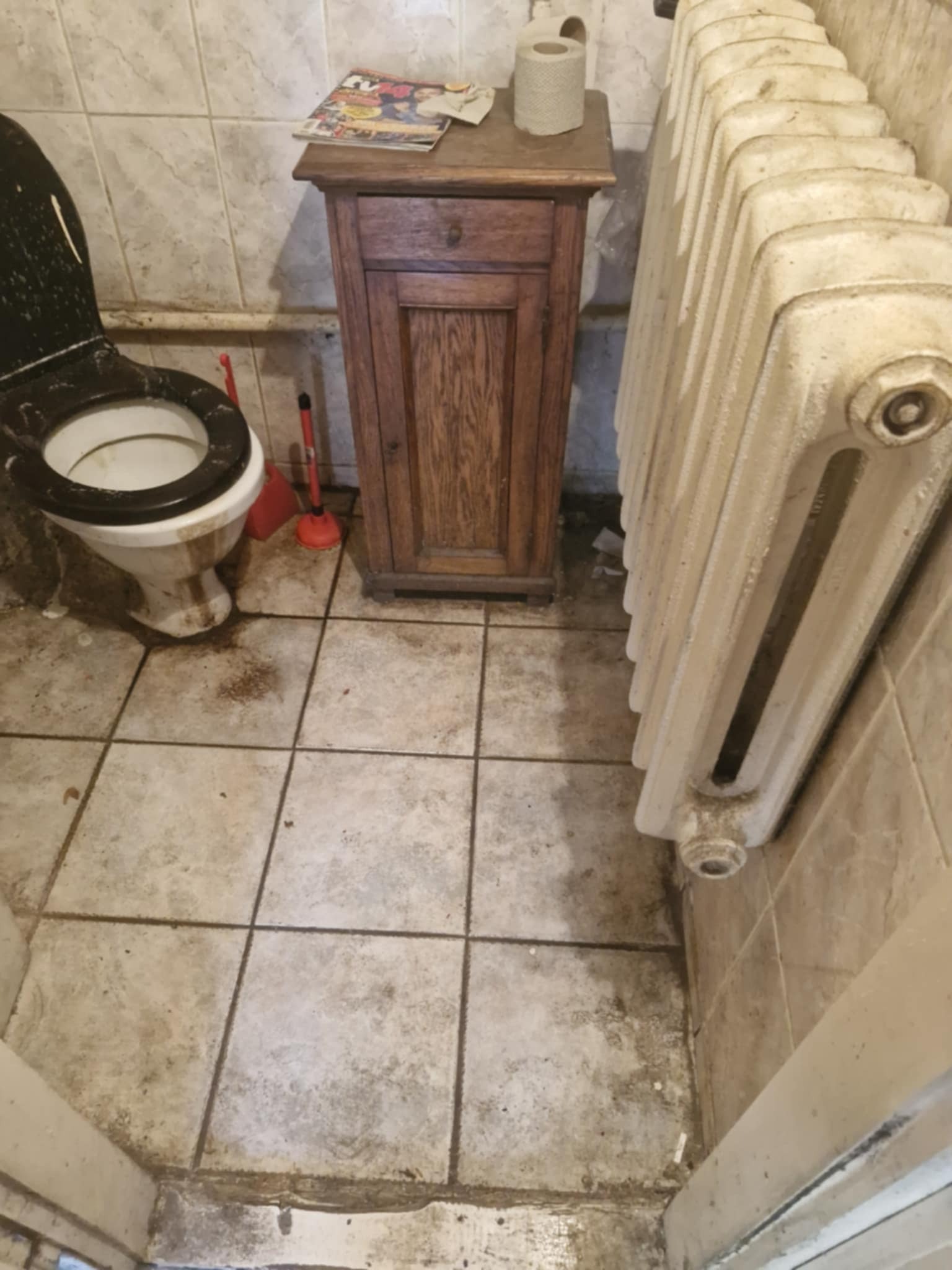 Zaniedbana łazienka z brudną toaletą, grzejnikiem i szafką. Widoczne zabrudzenia na podłodze i ścianach. Perspektywa z góry, podkreślająca stan pomieszczenia.