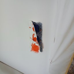 ELEKTROINSTAL ARW - Gniazdko elektryczne w ścianie, zabezpieczone taśmą malarską z fragmentami farby, widoczne ślady prac malarskich na ścianie i folia ochronna.