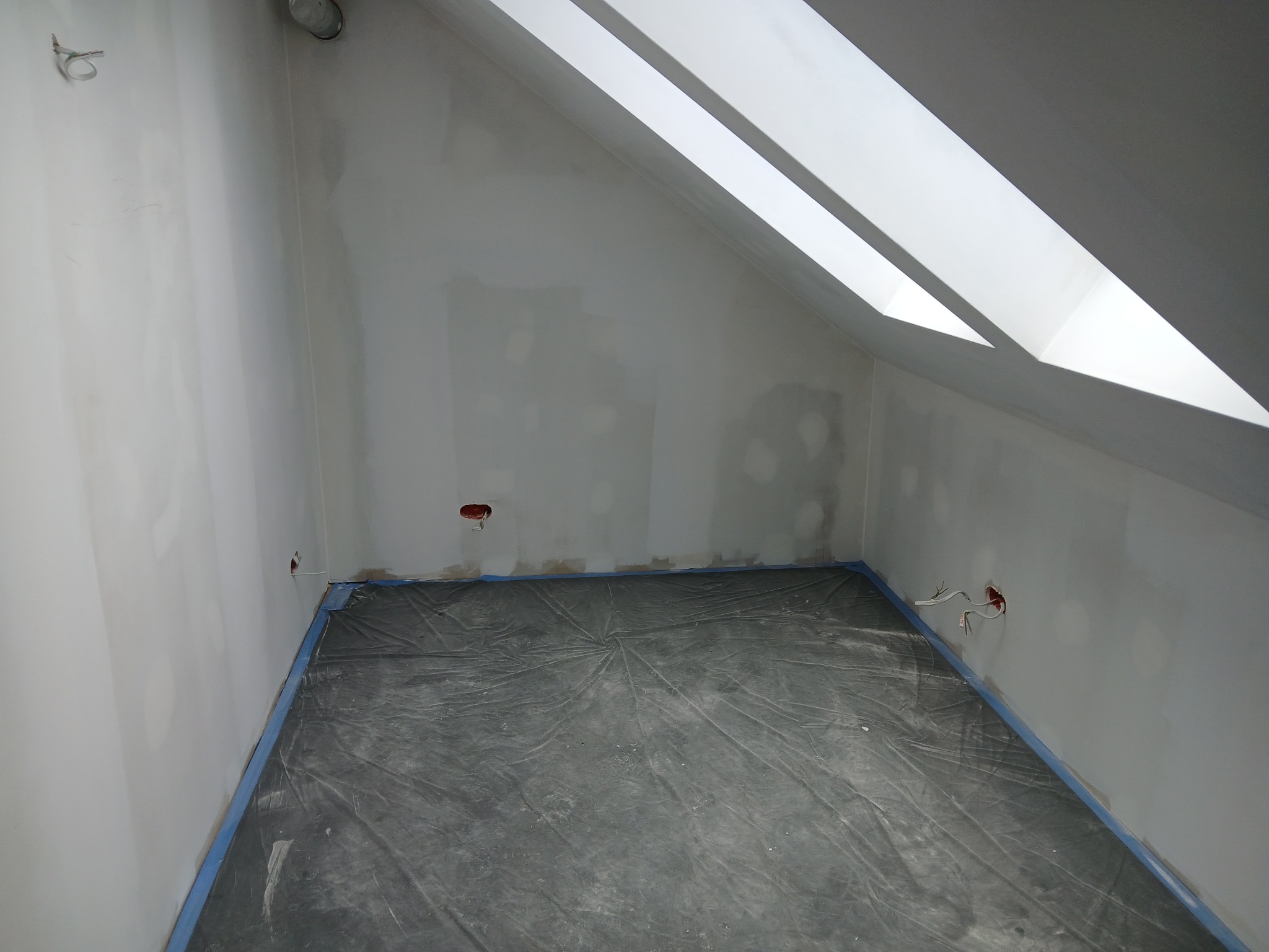 Poddasze w trakcie prac wykończeniowych: zabezpieczona folią podłoga, przygotowane punkty elektryczne w ścianach, okna dachowe w skosie.