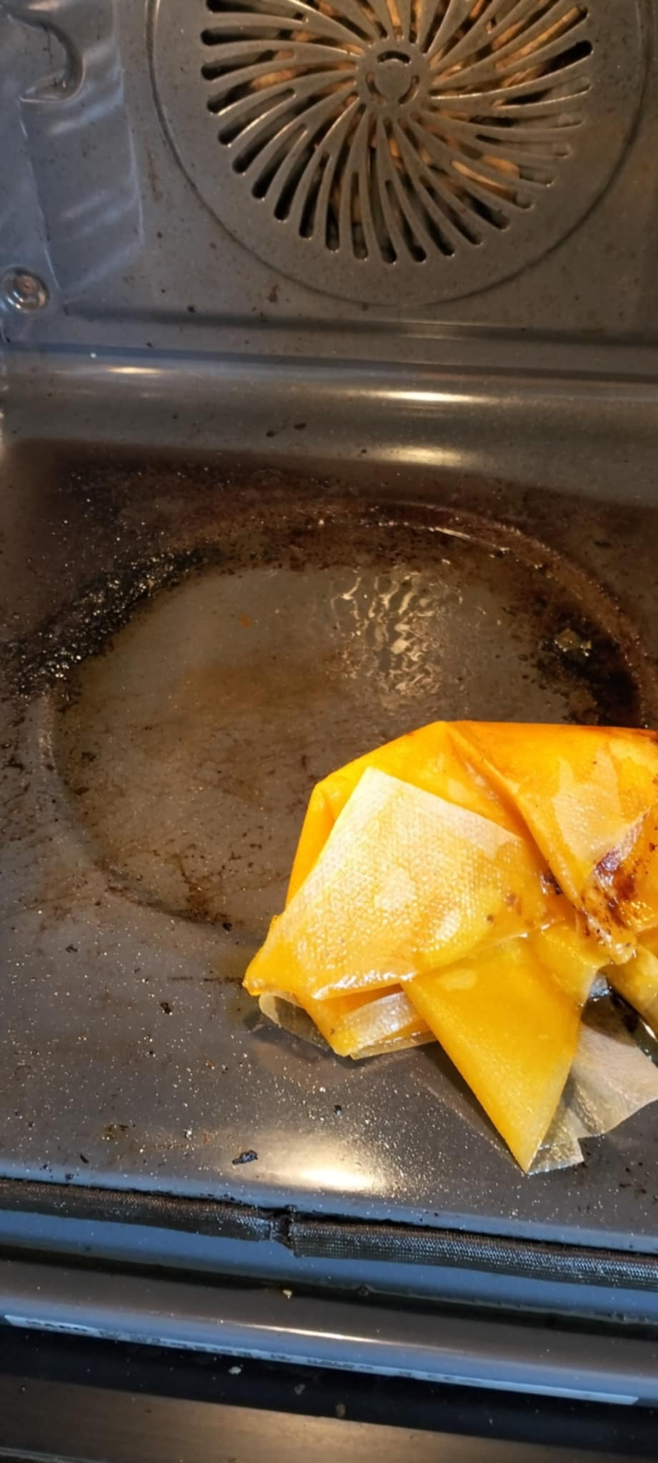 Wnętrze brudnego piekarnika z przypalonym tłuszczem i resztkami jedzenia, częściowo wytarte żółtą ścierką. Widoczne ślady użytkowania i zaniedbania.