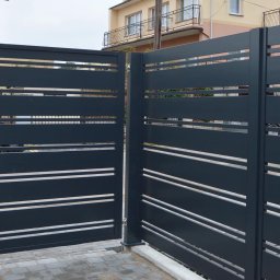 ZEGGER TECH SPÓŁKA Z OGRANICZONĄ ODPOWIEDZIALNOŚCIĄ - Nowoczesna, grafitowa brama wjazdowa z poziomymi, jasnymi prześwitami, częściowo otwarta, z widocznym fragmentem posesji i domu w tle.