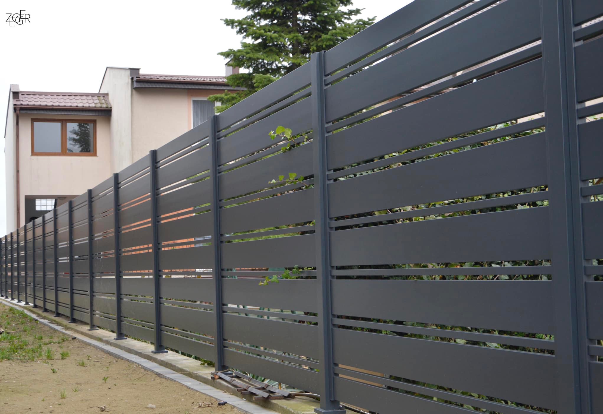 Nowoczesne, poziome przęsła ogrodzeniowe z metalu w kolorze grafitowym, z widocznymi prześwitami, na tle domu jednorodzinnego i zieleni.