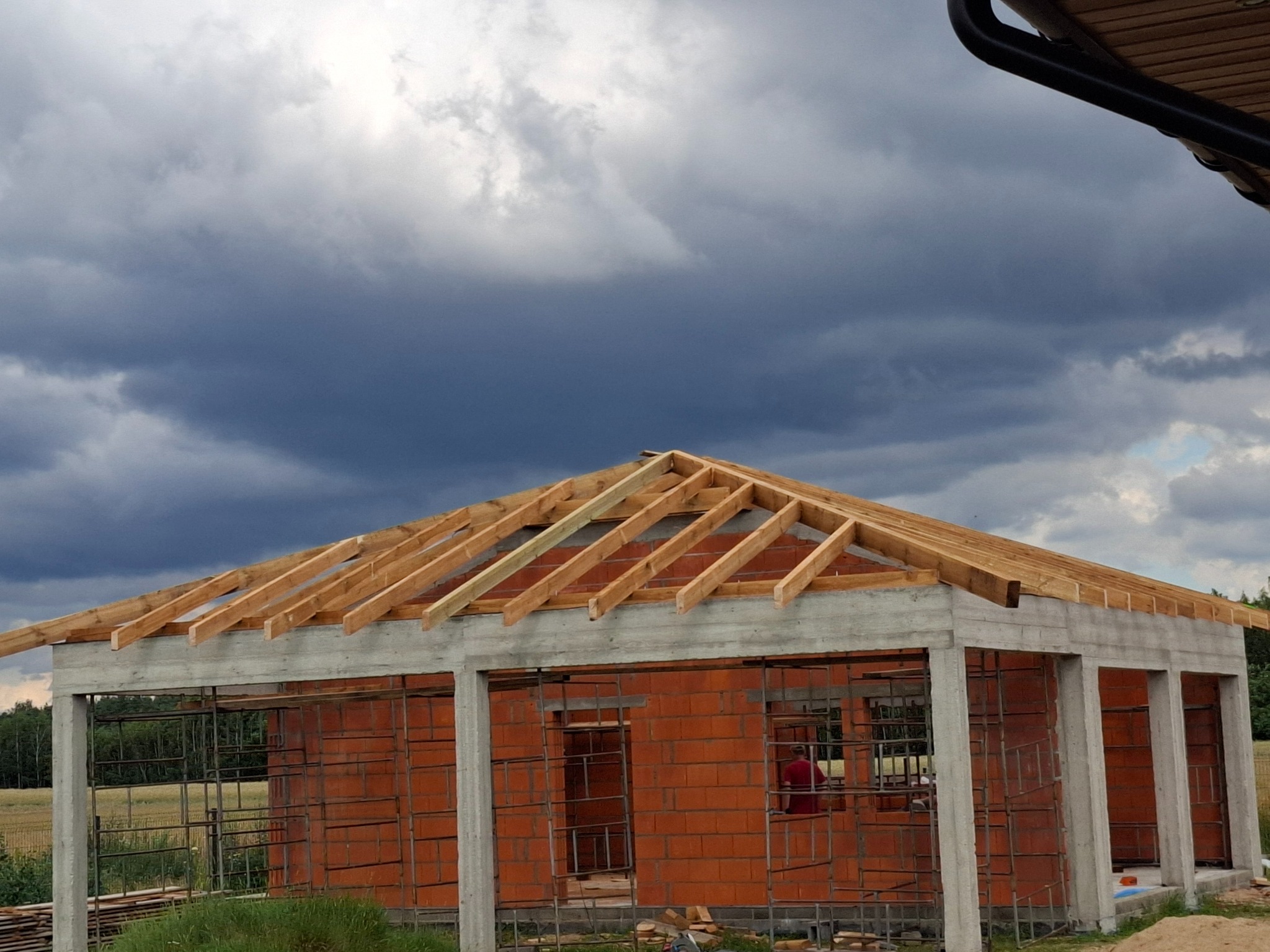 Budynek w trakcie budowy z widoczną więźbą dachową na tle burzowego nieba.