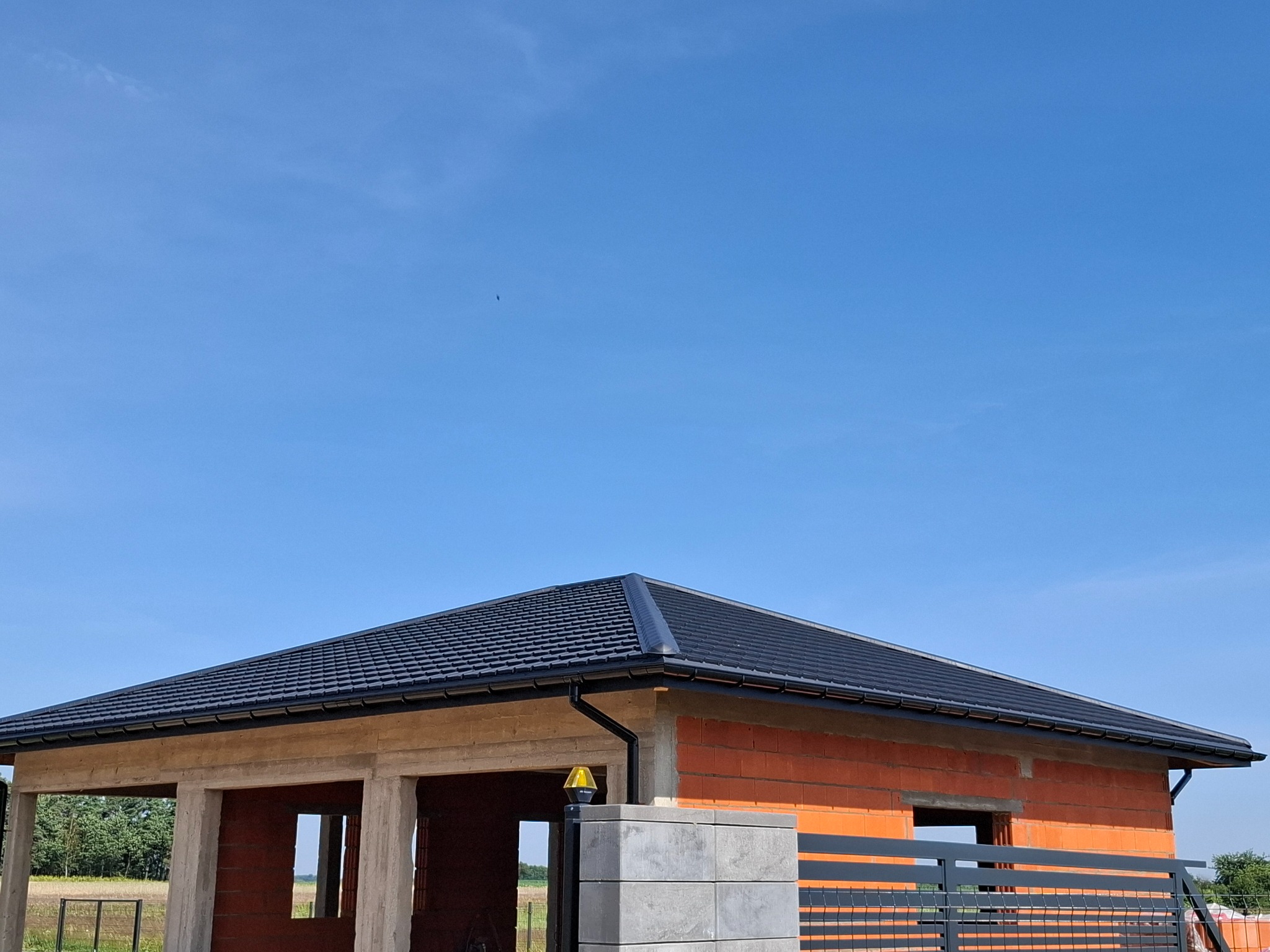 Nowy, czarny dach z rynnami na budynku w trakcie budowy, ceglana konstrukcja, błękitne niebo w tle.