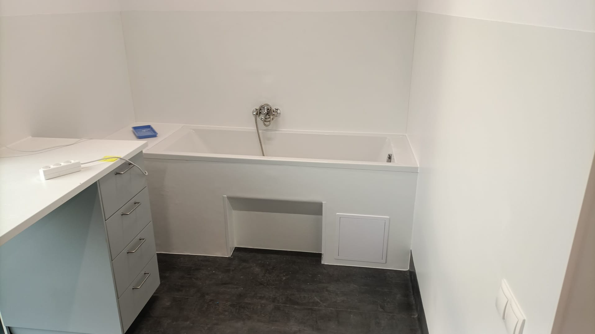 Wykończona sala laboratoryjna z wanną, ściany i podłoga pokryte okładzinami PCV, widoczna szafka z szufladami i przedłużacz na blacie.