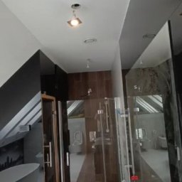 Paweł Szerszeń - Nowoczesna łazienka w trakcie wykańczania z białą umywalką nablatową, kabiną prysznicową ze szkła i drewnianymi elementami wykończeniowymi.