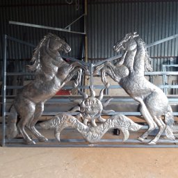 ADK blacksmith CNC Adam Kłos - Metalowa konstrukcja bramy z motywem dwóch wspiętych koni i słońca, wykonana przez firmę z Krakowa, widoczna w warsztacie.