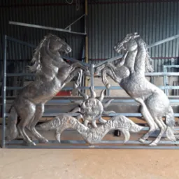 Metalowa konstrukcja bramy z motywem dwóch wspiętych koni i słońca, wykonana przez firmę z Krakowa, widoczna w warsztacie.