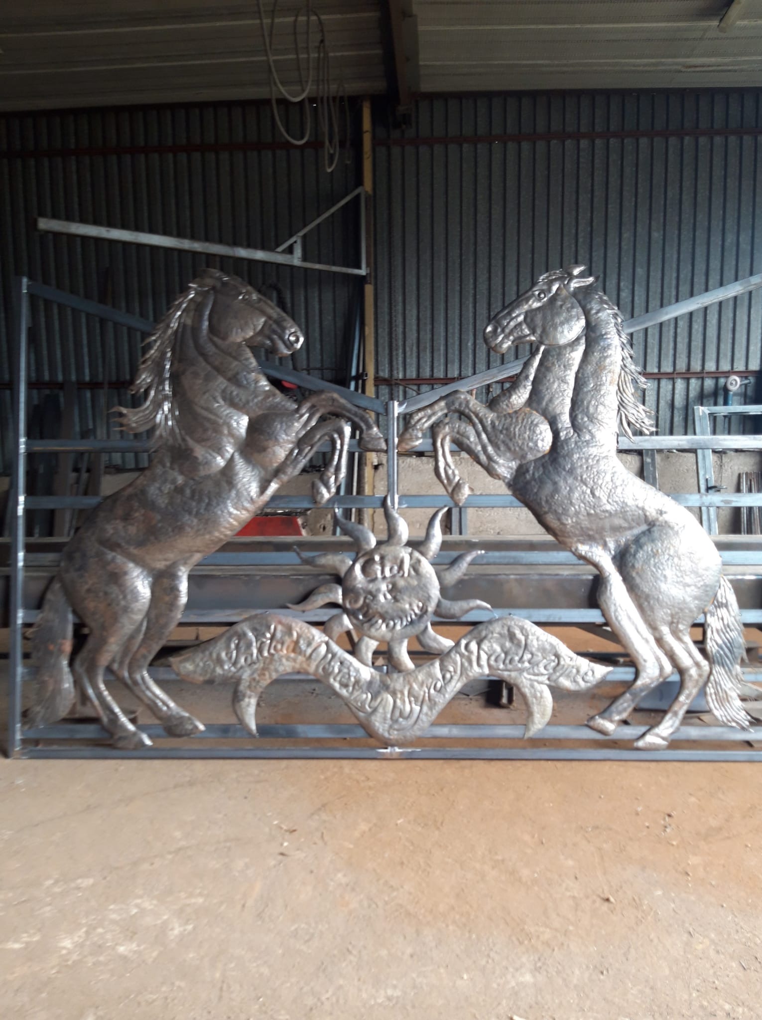 Metalowa konstrukcja bramy z motywem dwóch wspiętych koni i słońca, wykonana przez firmę z Krakowa, widoczna w warsztacie.