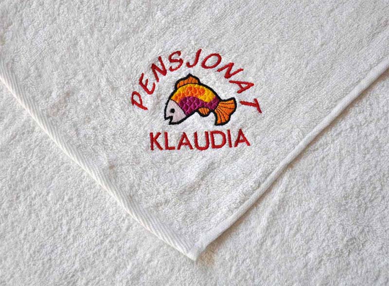 Biały ręcznik z wyhaftowanym kolorowym motywem ryby i napisem 'Pensjonat Klaudia'.