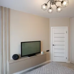 Nowoczesna sypialnia w beżowych tonacjach z podwieszaną szafką RTV, telewizorem, dekoracyjnym panelem ściennym z drewnianymi lamelami, białą, minimalistyczną drzwią i designerską lampą sufitową.