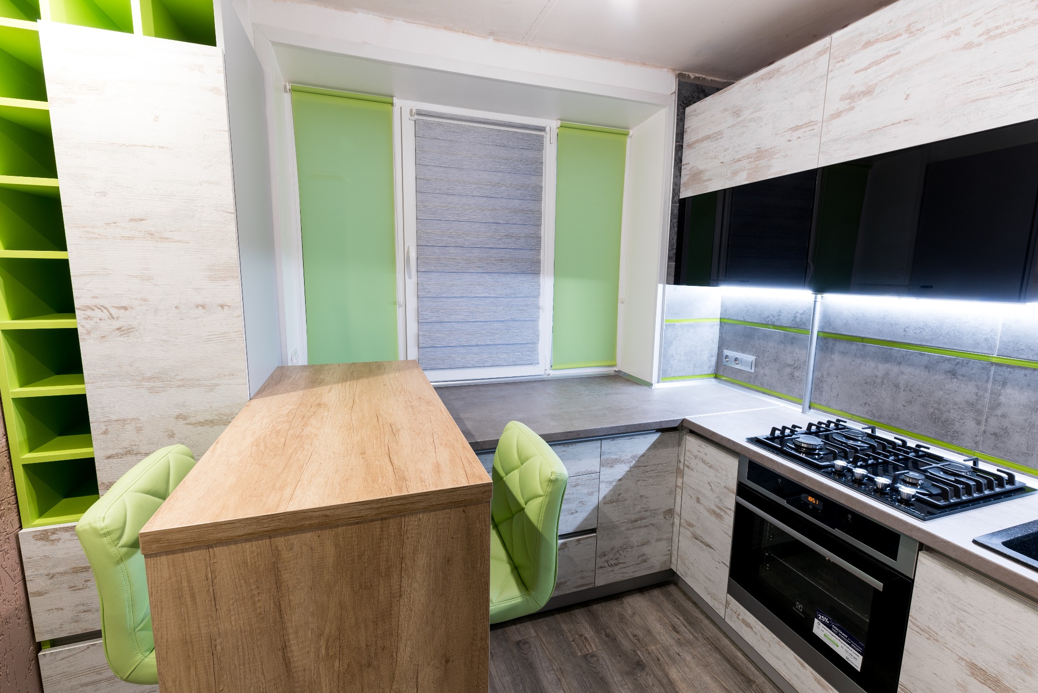 Nowoczesna kuchnia z drewnianym blatem, zielonymi akcentami i oknem z roletami w kolorze limonki, widok na płytę grzewczą i piekarnik.