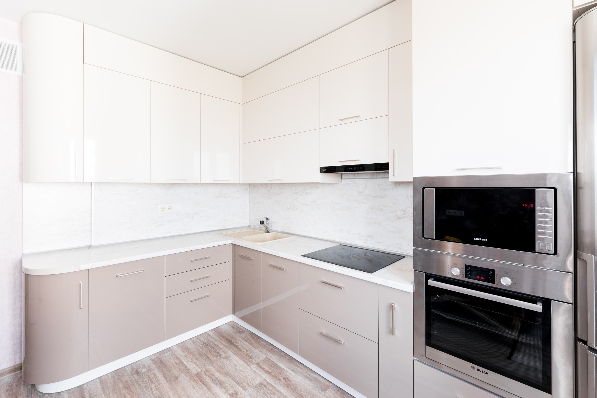 Jasna kuchnia z beżowymi dolnymi szafkami i białymi górnymi, z wbudowanym piekarnikiem i mikrofalówką oraz płytą indukcyjną.