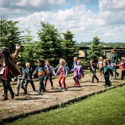 Agencja Turystyczno-Artystyczna Przygoda Anna Gołębiowska-Rusak - Grupa dzieci prowadzona przez animatora przebranego za pirata podczas zabawy na świeżym powietrzu.