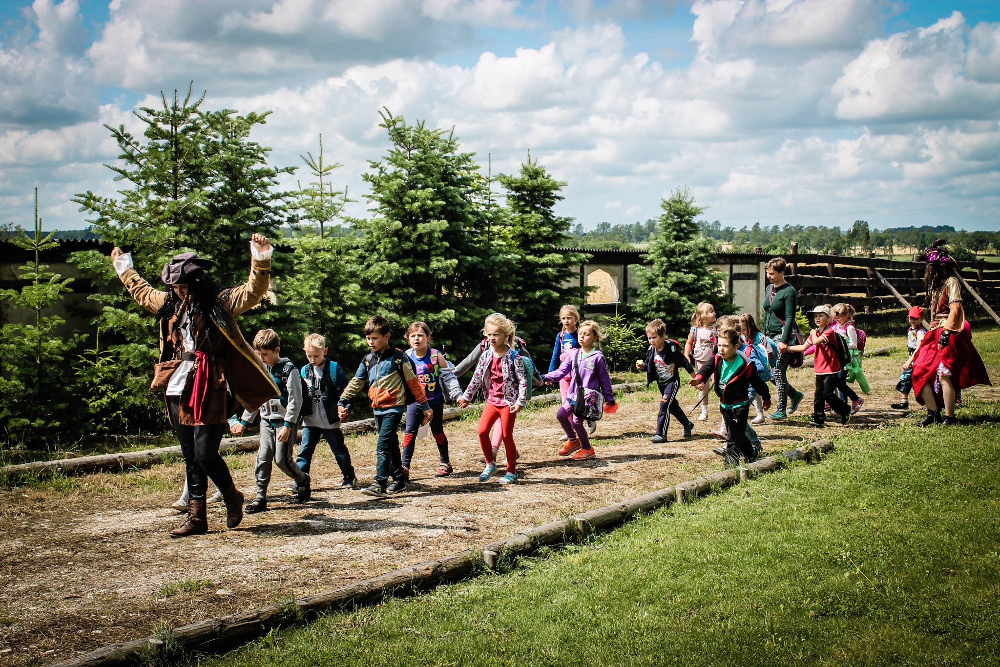 Grupa dzieci prowadzona przez animatora przebranego za pirata podczas zabawy na świeżym powietrzu.