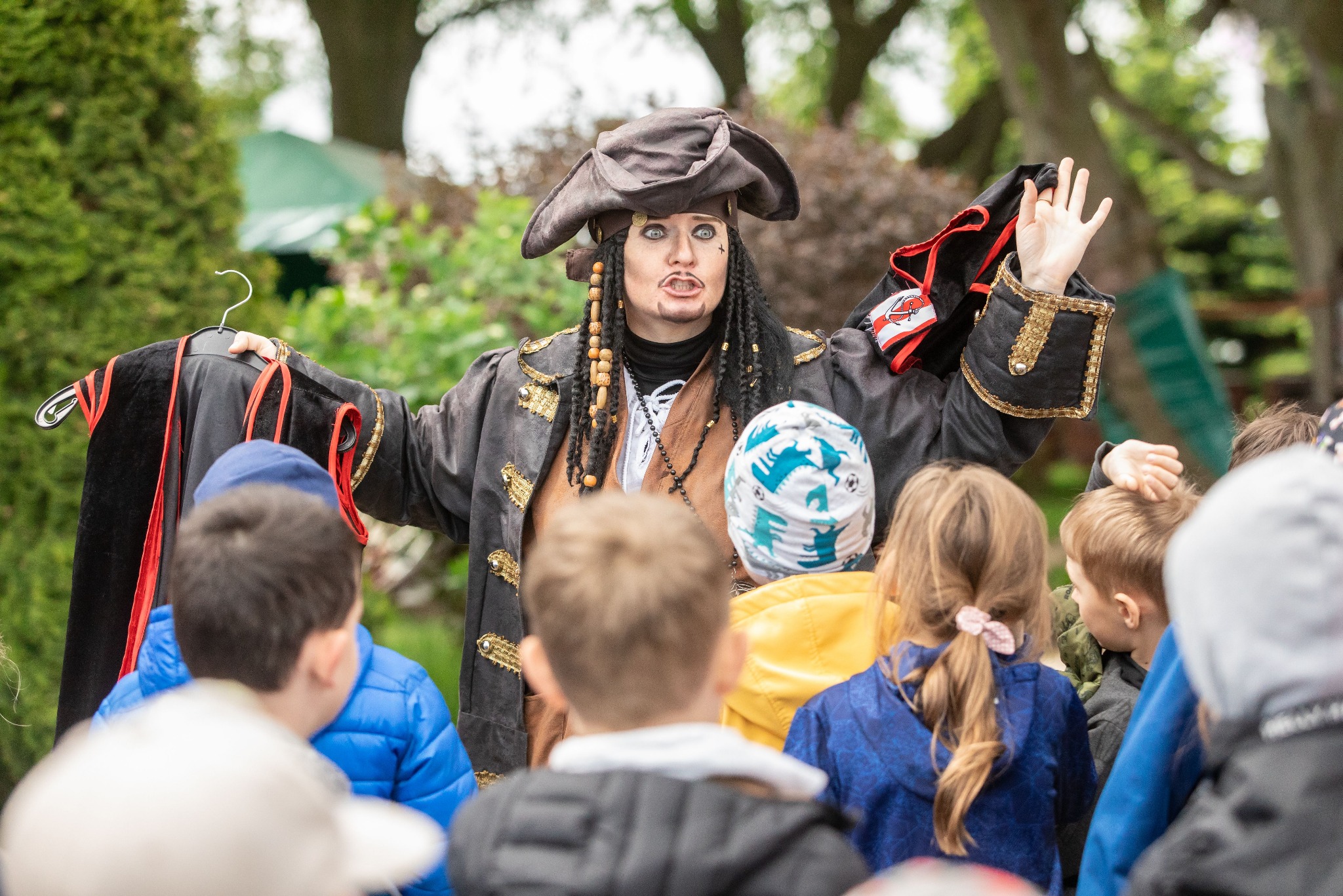 Osoba przebrana za pirata, z charakterystycznym makijażem i kostiumem, prezentuje strój dzieciom podczas wydarzenia plenerowego.