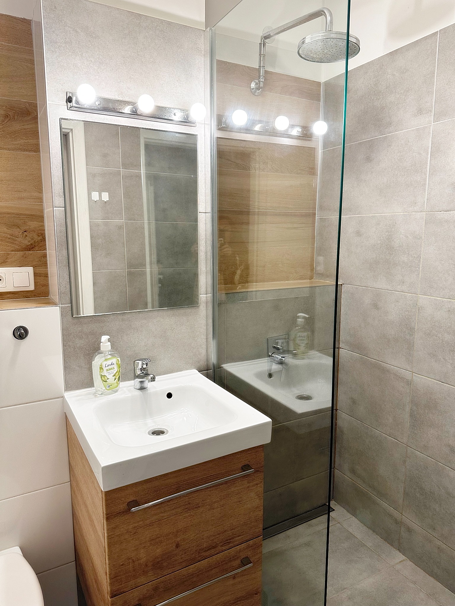 Nowoczesna łazienka w Warszawie z kabiną prysznicową typu walk-in, umywalką nablatową z szafką z drewnianym wykończeniem i dużym lustrem z oświetleniem.