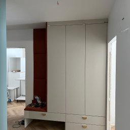 LenArt - Meble na wymiar Grzegorz Lenart - Montaż szafy wnękowej z siedziskiem w trakcie realizacji, widoczne narzędzia i elementy wykończeniowe na siedzisku, parkiet w jodełkę.