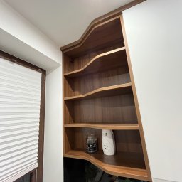 LenArt - Meble na wymiar Grzegorz Lenart - Półki z ciemnego drewna o falistych krawędziach, wkomponowane w białą zabudowę kuchenną, obok okna z żaluzjami.