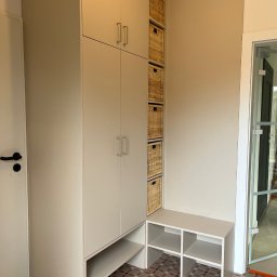 LenArt - Meble na wymiar Grzegorz Lenart - Jasna zabudowa meblowa z szafkami i wiklinowymi koszami, uzupełniona niską szafką z półkami, na tle wzorzystej podłogi i przeszklonych drzwi.