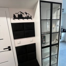 LenArt - Meble na wymiar Grzegorz Lenart - Biała zabudowa meblowa z czarnymi akcentami: przeszklona witryna z czarnymi szprosami, siedzisko z czarnych paneli tapicerowanych, dekoracja ścienna z motywem górskim.