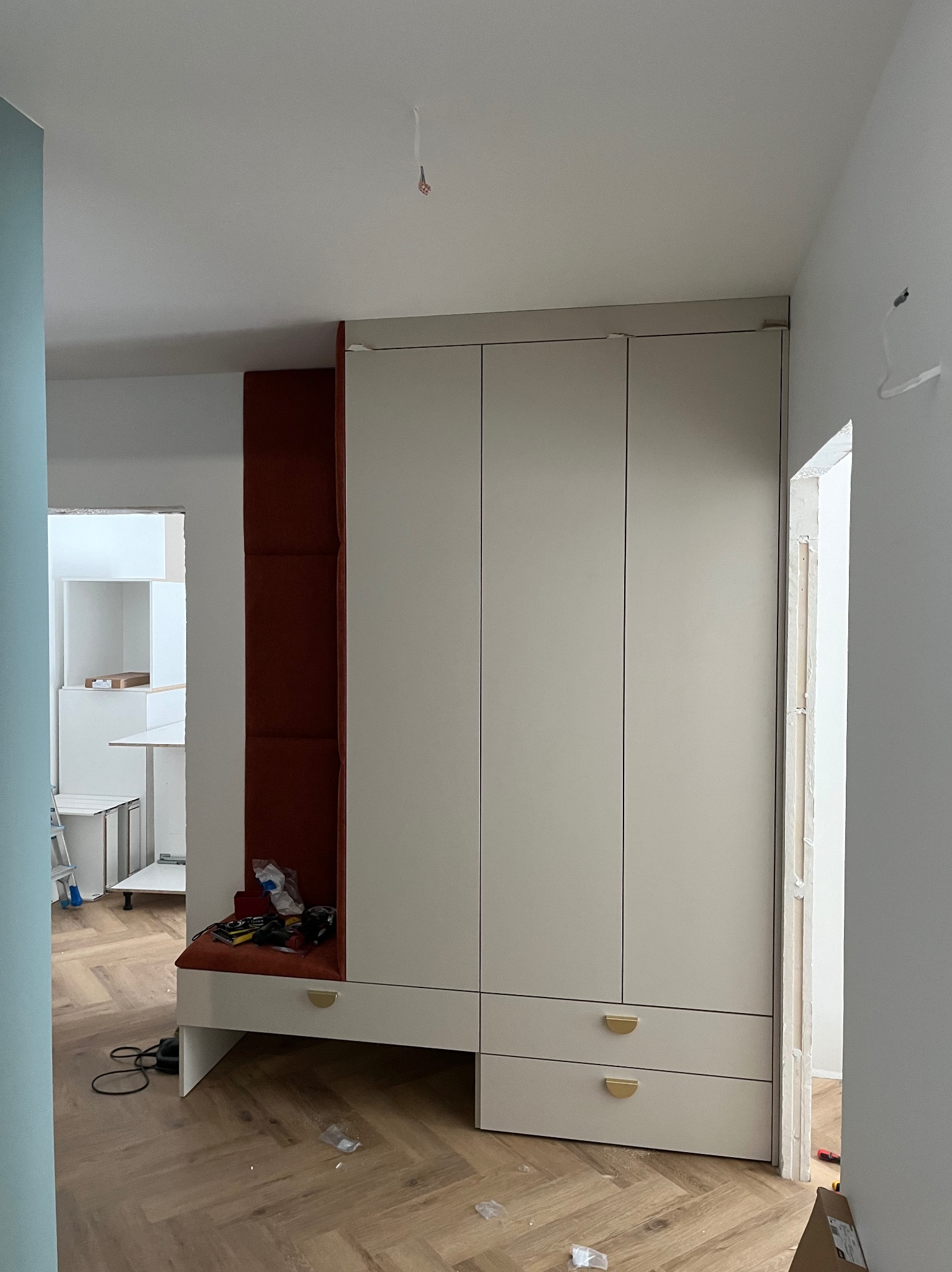 Montaż szafy wnękowej z siedziskiem w trakcie realizacji, widoczne narzędzia i elementy wykończeniowe na siedzisku, parkiet w jodełkę.