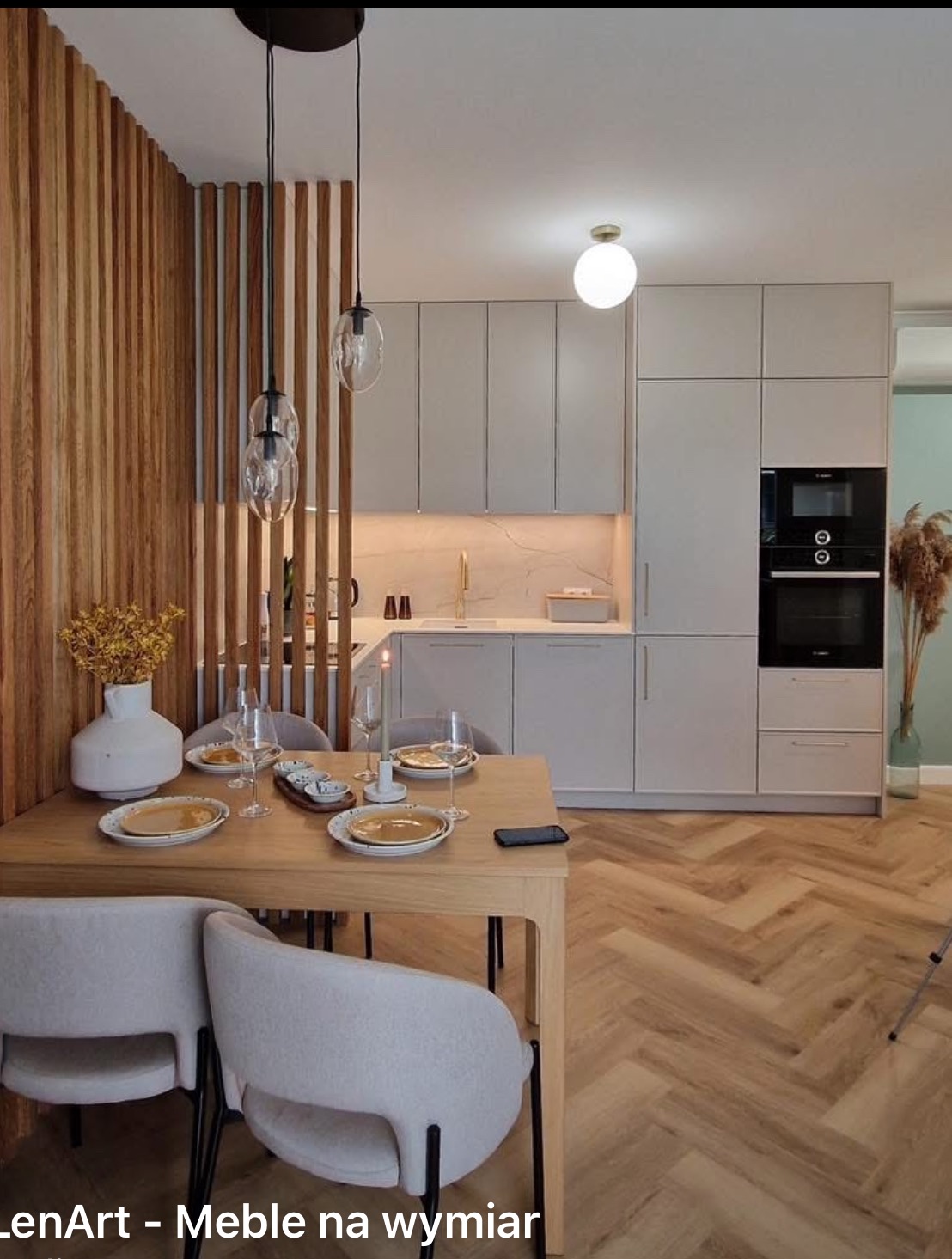 Jasna kuchnia z zabudową meblową i drewnianą ażurową ścianką działową, stół z nakryciem i krzesłami w stylu skandynawskim, parkiet w jodełkę.