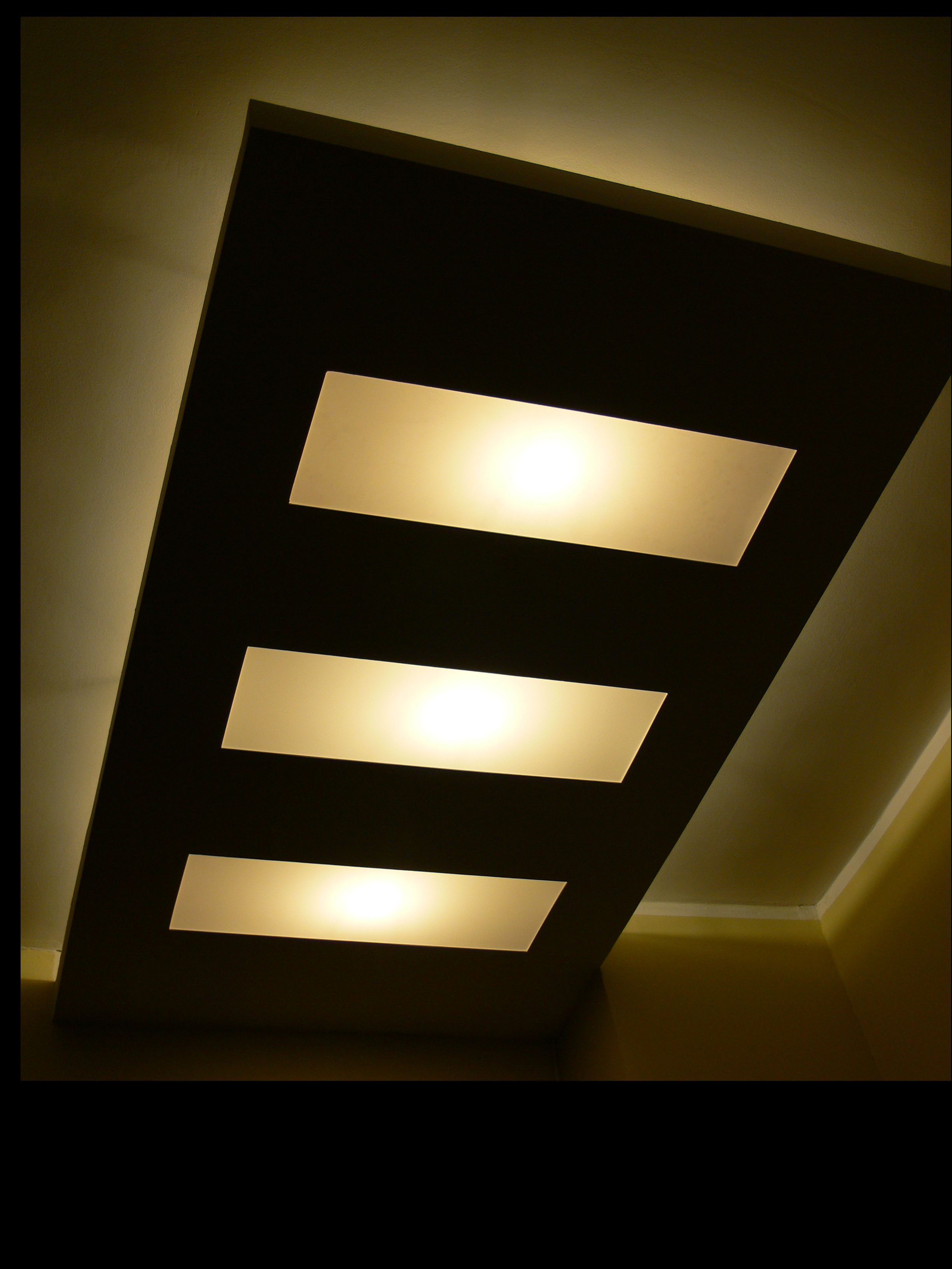 Sufit podwieszany z trzema prostokątnymi panelami świetlnymi, oświetlenie punktowe w nowoczesnym stylu, ciepła barwa światła.