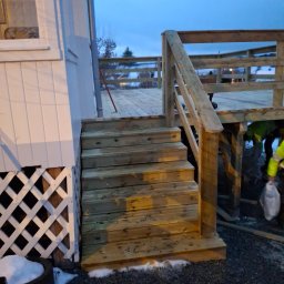 Mikołaj Kulig - Nowo wybudowany taras drewniany z schodami przylegający do białego domu z kratownicą, widoczne elementy konstrukcyjne, częściowo ośnieżony teren i pracownik w odblaskowej kamizelce w tle.