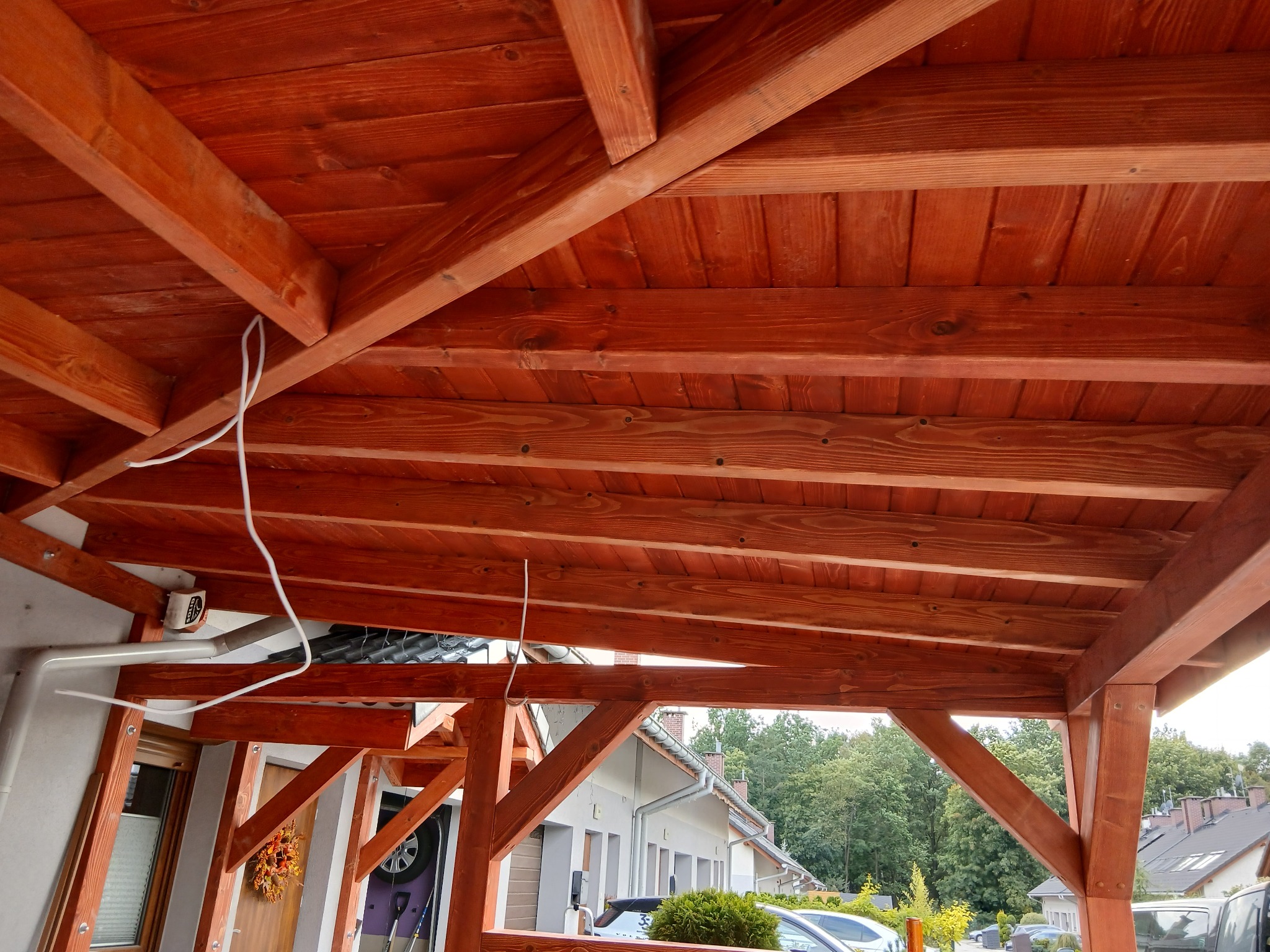 Drewniana konstrukcja z belek w kolorze brązowym, prawdopodobnie zadaszenie tarasu lub altany, widok z dołu, z elementami instalacji elektrycznej.