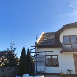 Usługi dekarskie - Dom jednorodzinny w trakcie prac dekarskich, widoczne rusztowania, częściowo zdjęte stare pokrycie dachu i ułożona nowa dachówka w kolorze grafitowym, na dole ułożone bloczki styropianowe.