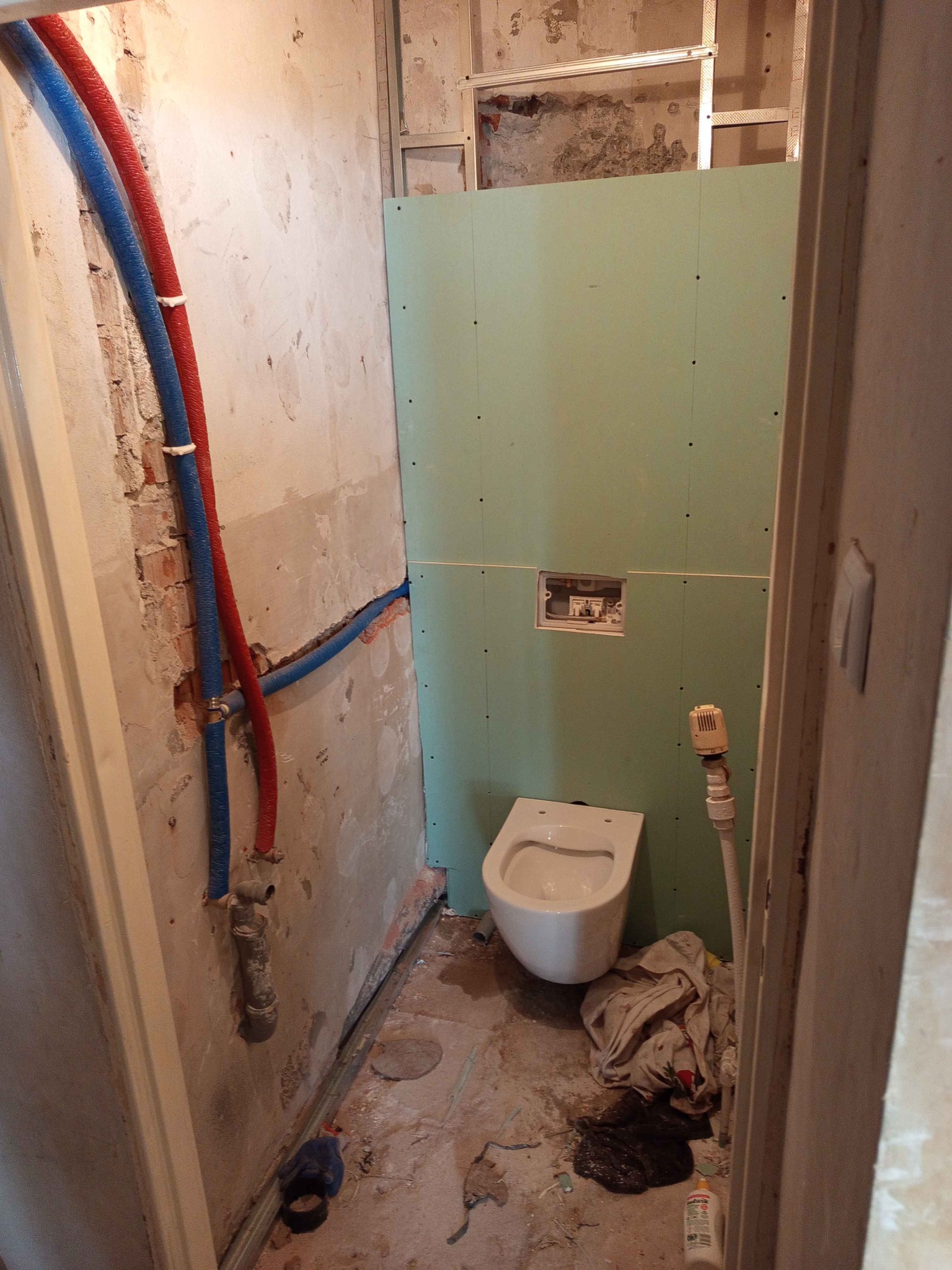Łazienka w trakcie remontu: podwieszana toaleta, instalacja wodna z rurami w izolacji, ściany częściowo wykończone płytami gipsowo-kartonowymi, widoczne przewody instalacji.